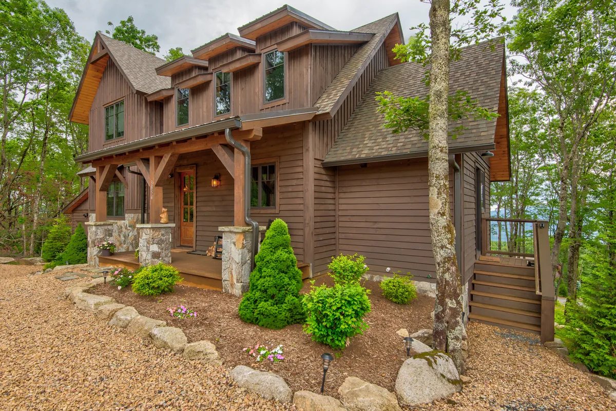 This exterior image captures the inviting wooden front door of Grayling Lodge, framed by stone accents, a beautifully landscaped garden, and large windows. The porch space suggests outdoor relaxation, with ample opportunity for gatherings and enjoying nature.