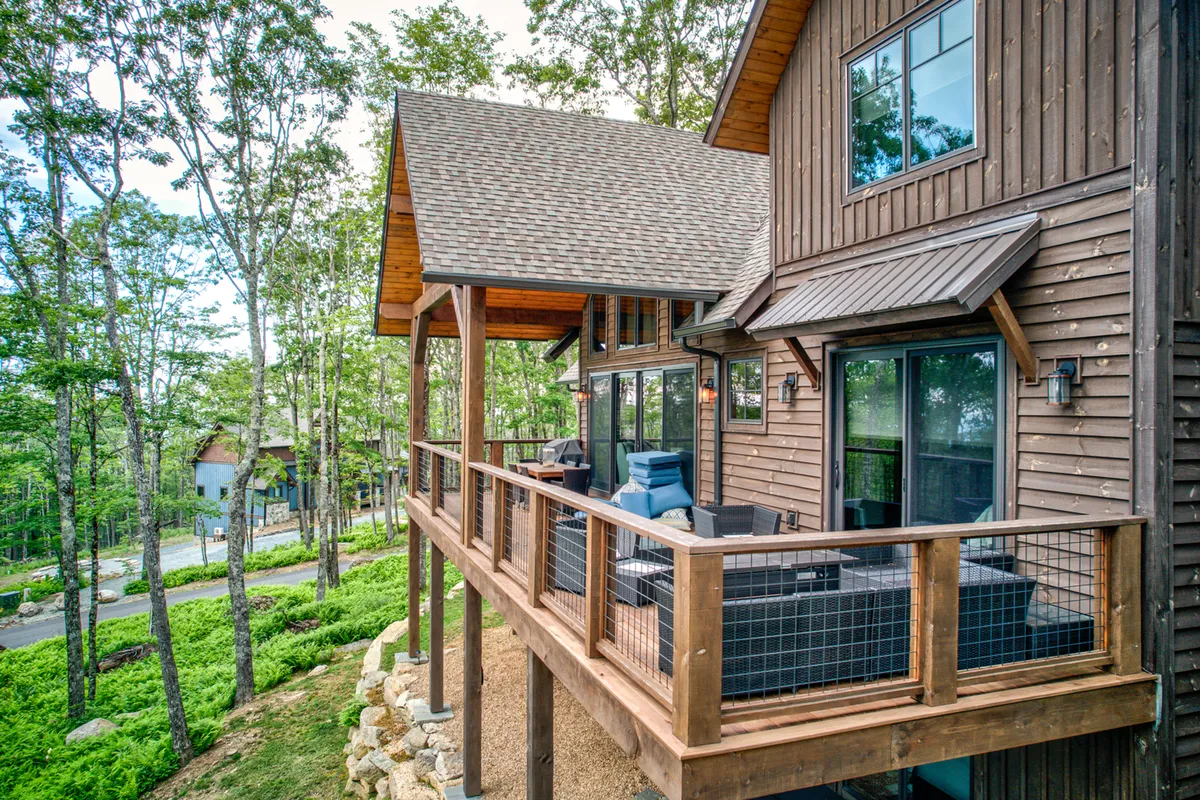 This exterior shot displays a wooden deck with an outdoor seating area, surrounded by trees and natural stone accents. The peaceful ambiance and comfortable furnishings encourage both quiet reflection and entertaining guests amid nature.