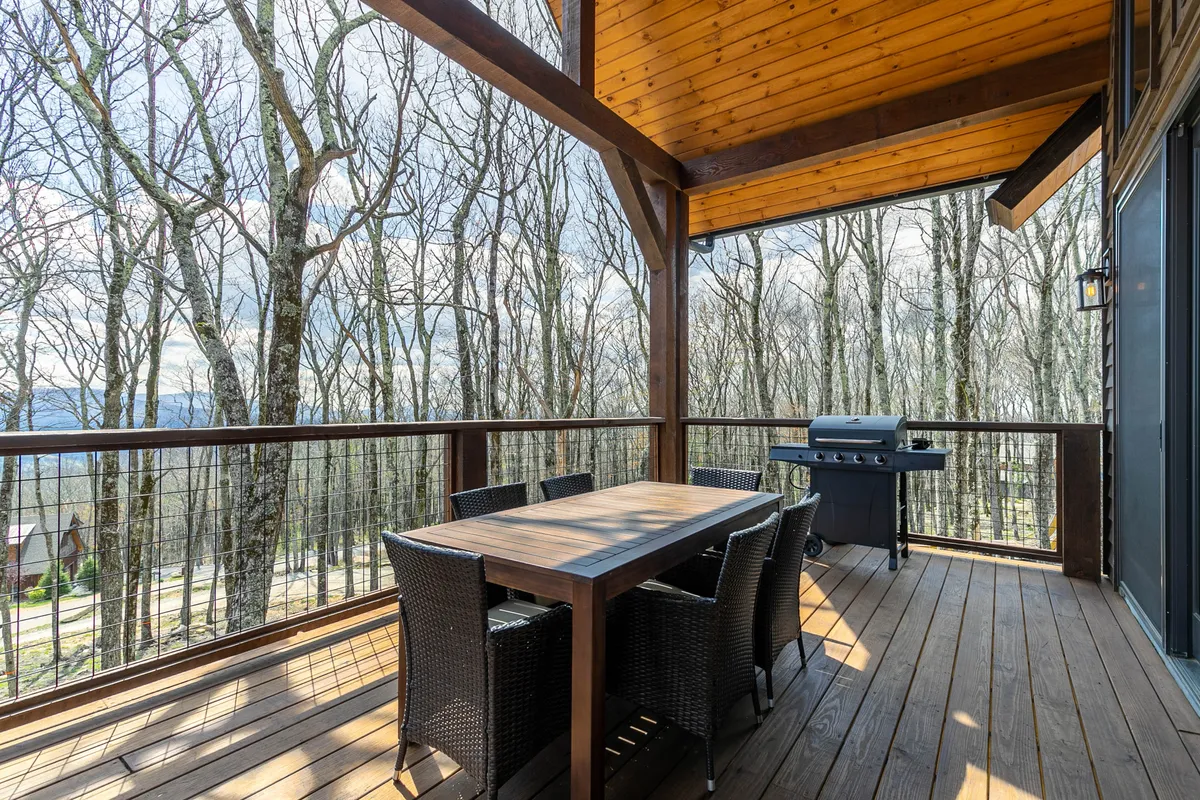A serene outdoor dining area with a table and grill set against a backdrop of trees, offering a glimpse of the surrounding natural beauty. The space invites social gatherings, barbecues, and shared meals in a tranquil setting.