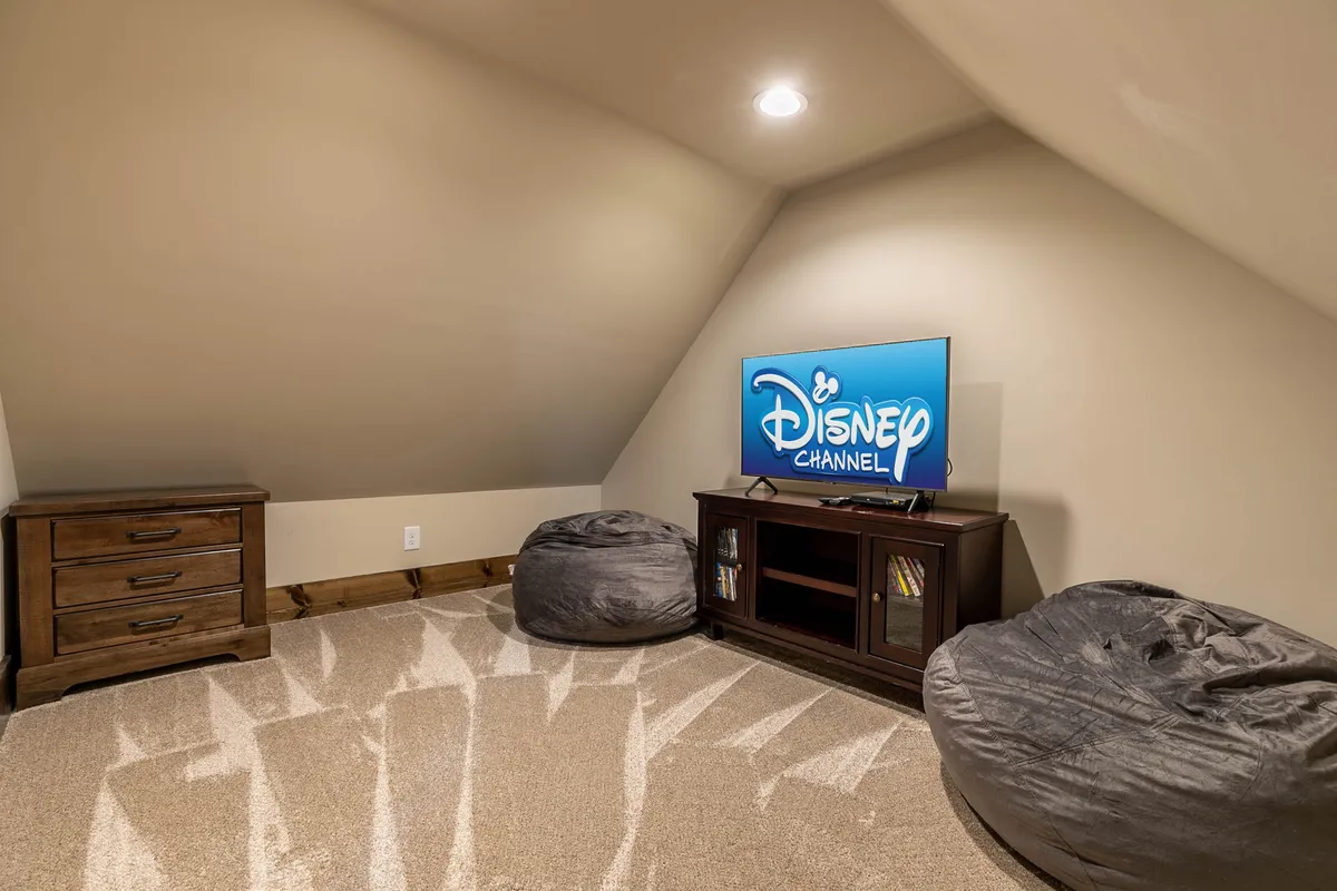 A cozy entertainment area with a large television displaying Disney Channel, colorful bean bag chairs, and a wooden dresser. The playful seating and relaxed setup suggest a perfect spot for movie nights or gaming sessions, appealing to all ages.