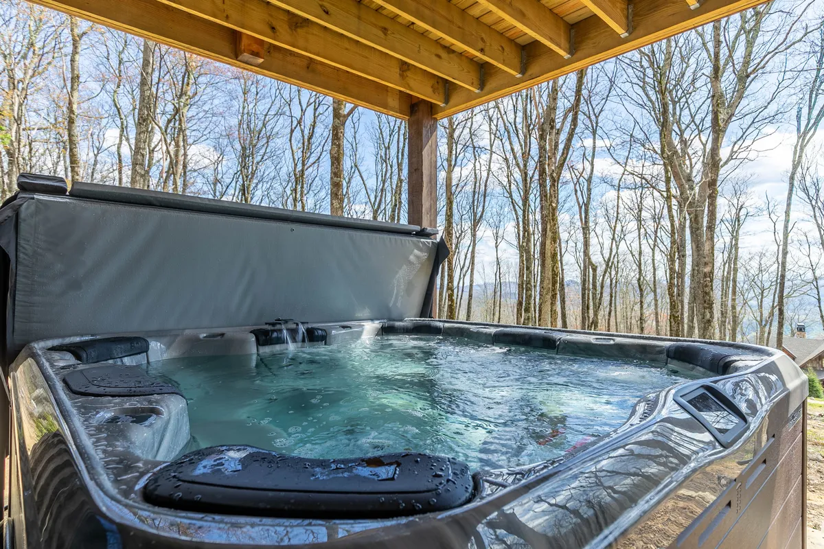 A tranquil hot tub situated on a deck, surrounded by trees with mountain views in the distance. The scene exudes peaceful relaxation, perfect for stargazing or unwinding after a mountain adventure.