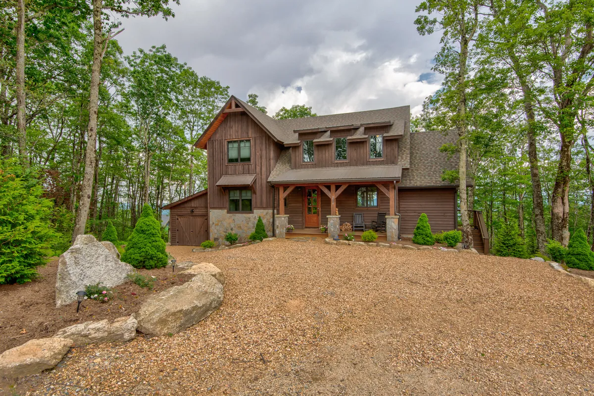 The photograph features the lodge's spacious front porch, stone pathway, and lush landscaped garden, offering a tranquil setting surrounded by greenery. The porch and garden are ideal for relaxing, hosting gatherings, or simply enjoying the changing mountain scenery throughout the year.