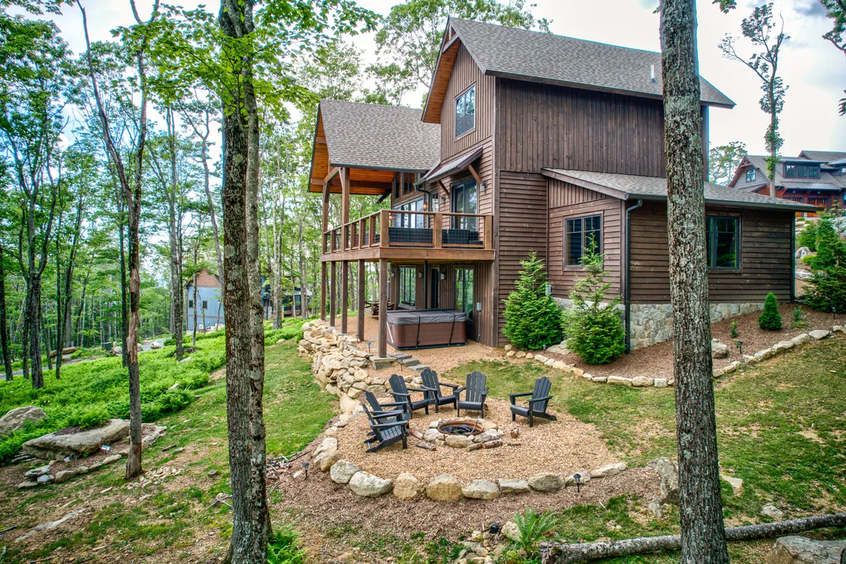 An inviting exterior view of a wooden cabin structure with a cozy fire pit surrounded by seating, set in lush greenery. Guests are pictured gathering around the fire, relaxing on the balcony, and exploring the wooded surroundings, evoking a sense of camaraderie and post-adventure relaxation.