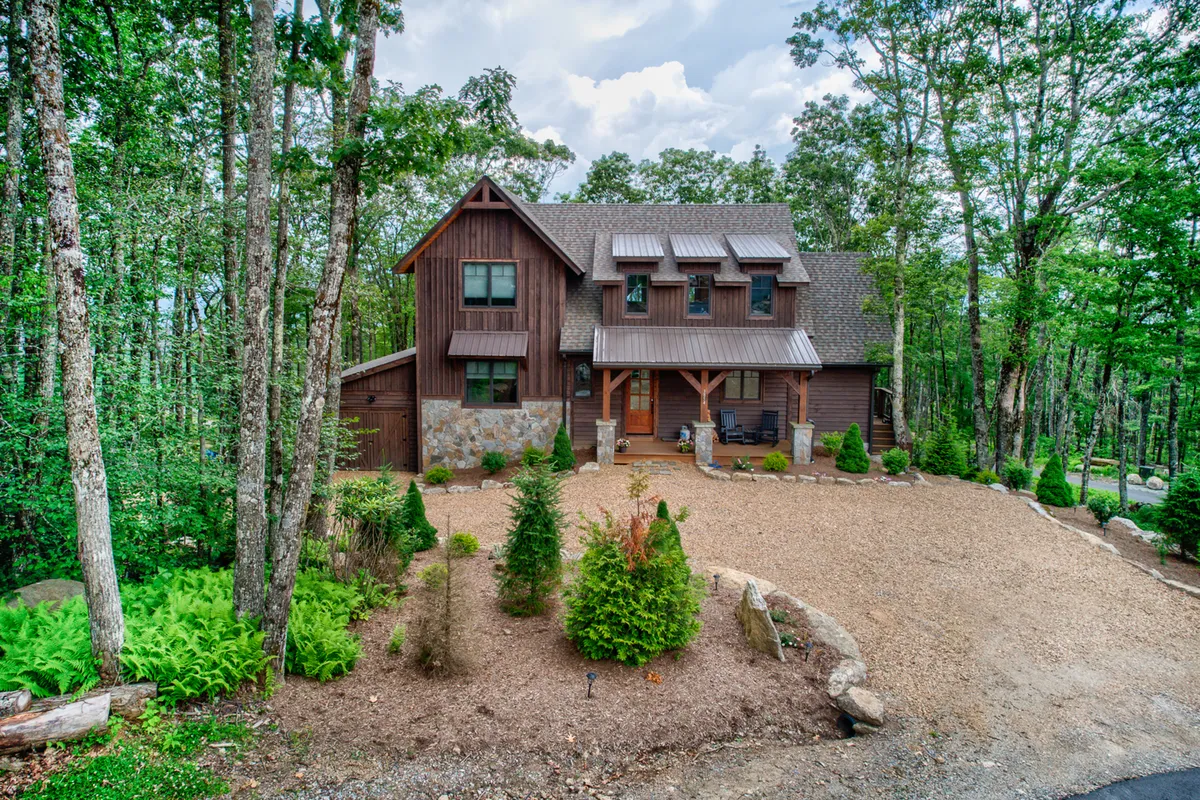 The hero image showcases the rustic wooden facade of Grayling Lodge, accented by natural stonework and surrounded by a beautifully landscaped garden. The spacious porch invites guests to relax and enjoy the serene mountain setting, while the lush greenery hints at abundant opportunities for outdoor activities and family gatherings.
