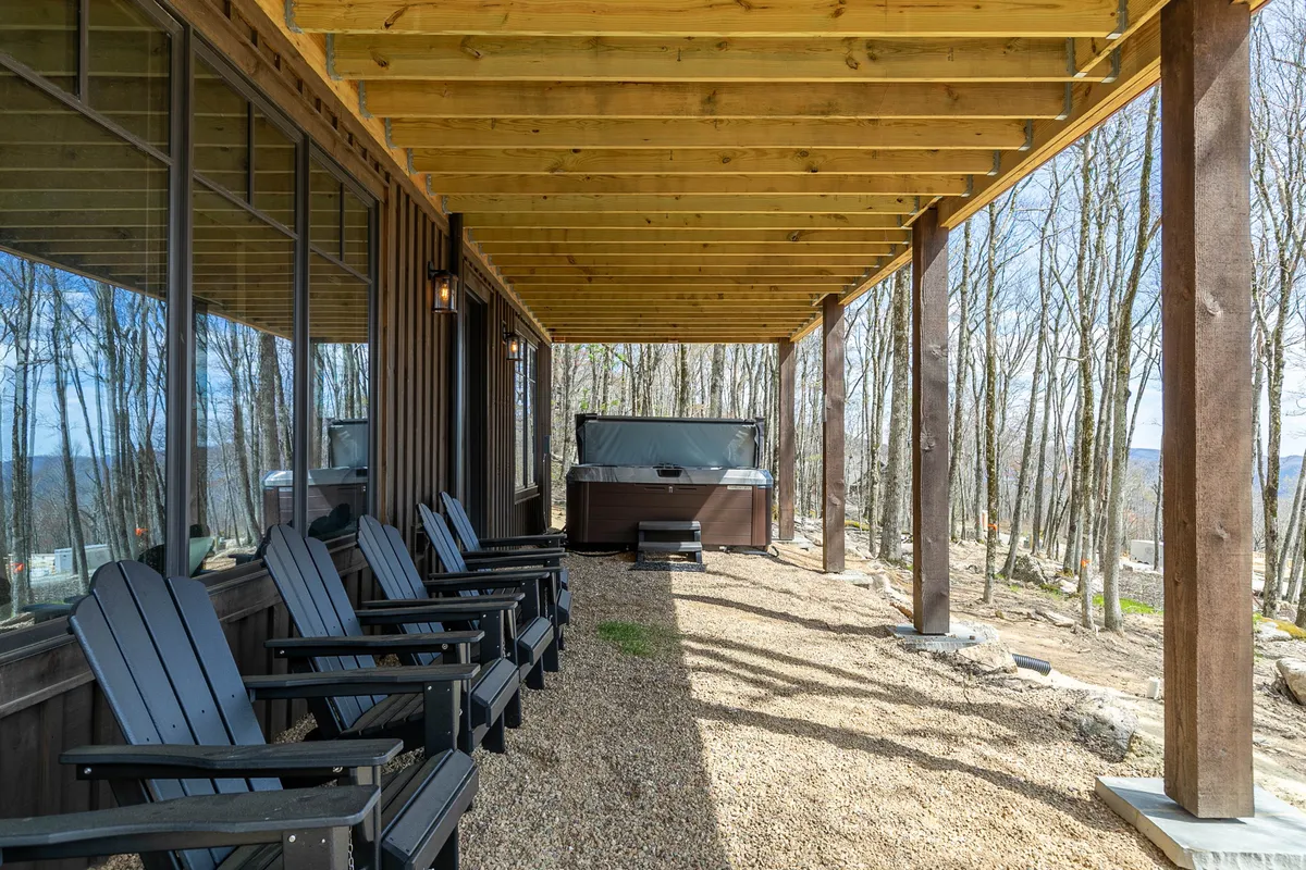 This image features a tranquil outdoor setting with a hot tub and wooden chairs positioned to overlook a scenic tree line. The natural deck setting evokes relaxation and luxury, ideal for socializing or unwinding while immersed in the surrounding landscape.