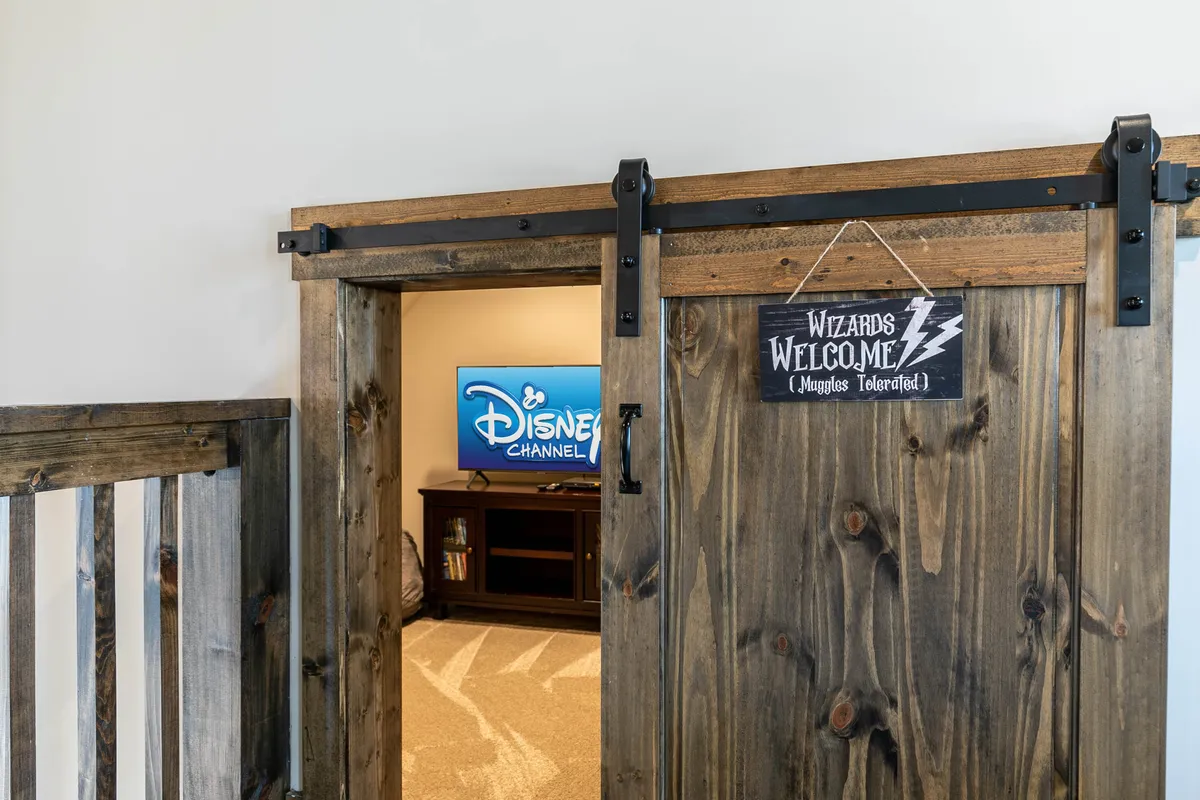 A whimsical nook with a wooden sliding barn door, a TV displaying the Disney Channel, and a 'Wizards Welcome' sign, all contributing to a playful, magical atmosphere perfect for kids and Harry Potter fans alike.