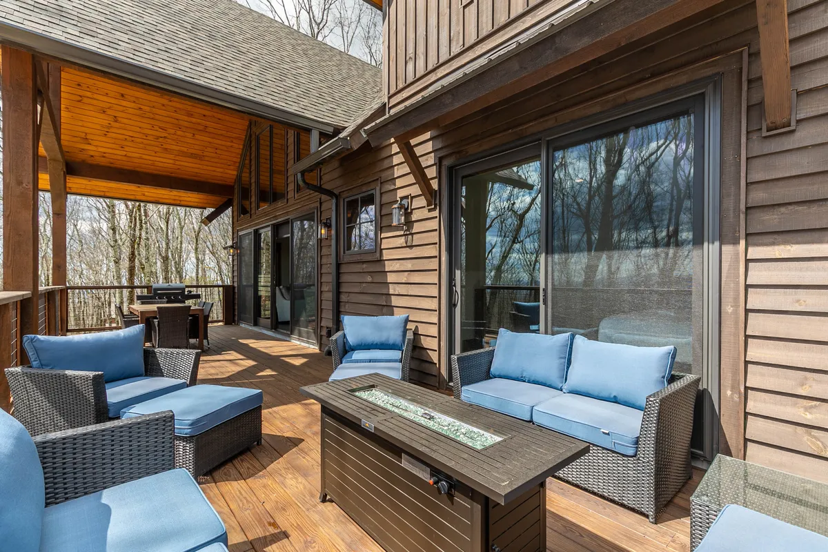 An inviting exterior shows a wooden deck with a comfortable seating area and coffee table, set against a backdrop of lush greenery. The space is designed for relaxation, socializing, and enjoying the outdoors, whether for coffee in the morning or gathering at sunset.
